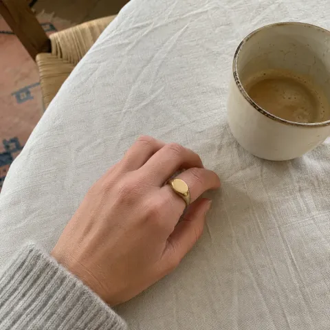 Foto de una mano con un anillo dorado junto a un café (tienda ficticia Doria)